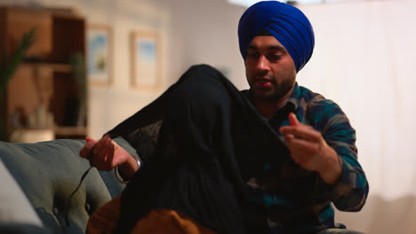 Vater-Bindet-Seinem-Jungen-Sikh-Sohn-Mit-Haarknoten-Einen-Turban-Um-Den-Kopf,-Der-Zu-Hause-Auf-Dem-Sofa-Sitzt-–-Aufnahme-In-Echtzeit